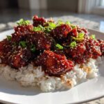 Close-up of Sticky Sweet Chili Chicken Skillet pieces coated in dark glaze, served over white rice and garnished with sesame seeds and green onions.