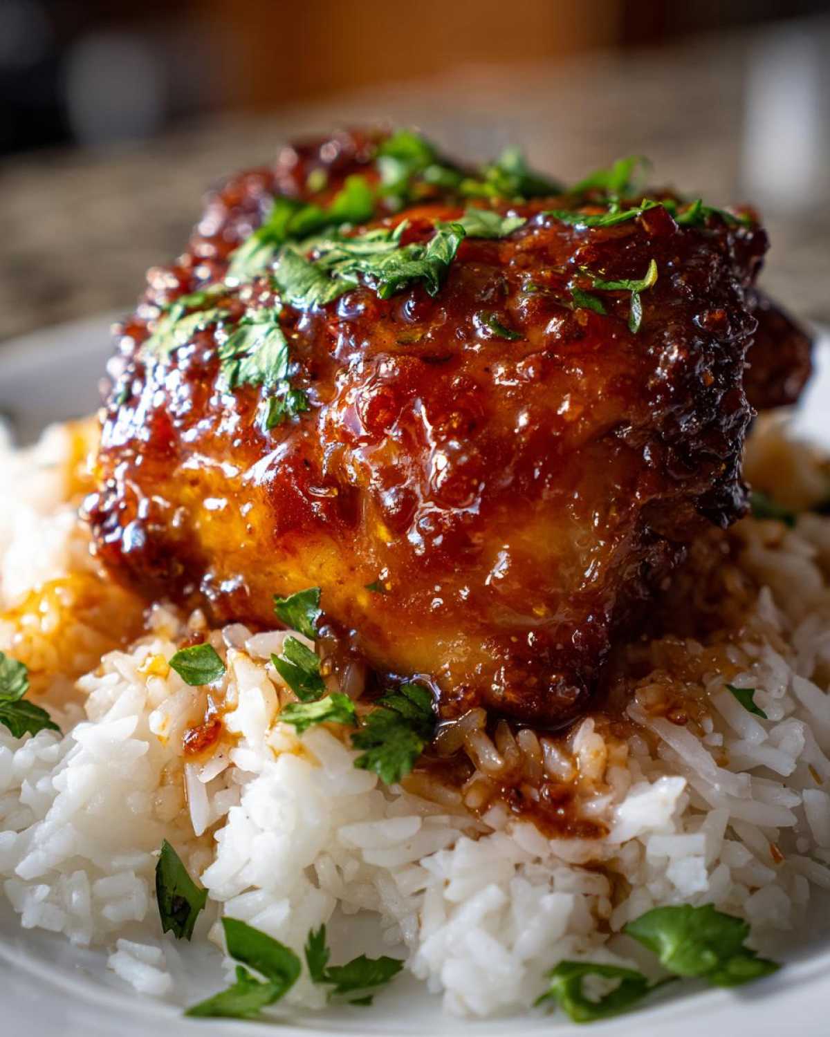 A close-up of a Sticky Sweet Chili Chicken Thighs coated in glossy sauce, resting on a bed of white rice and garnished with cilantro.