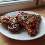 Two pieces of Sticky Teriyaki Chicken Thighs with Garlic, glazed and topped with sesame seeds on a white plate.